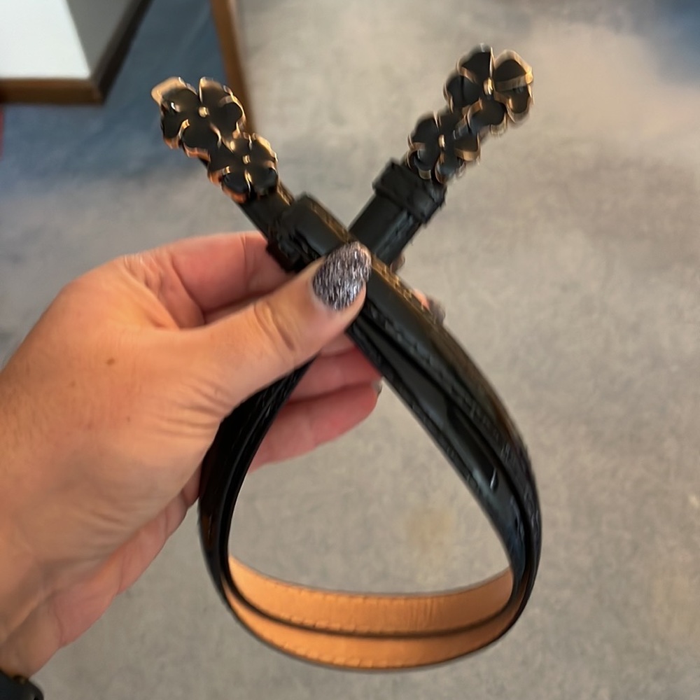 Shiny black fashion belt with clasp and decorative black flowers. Fits size 0-8.